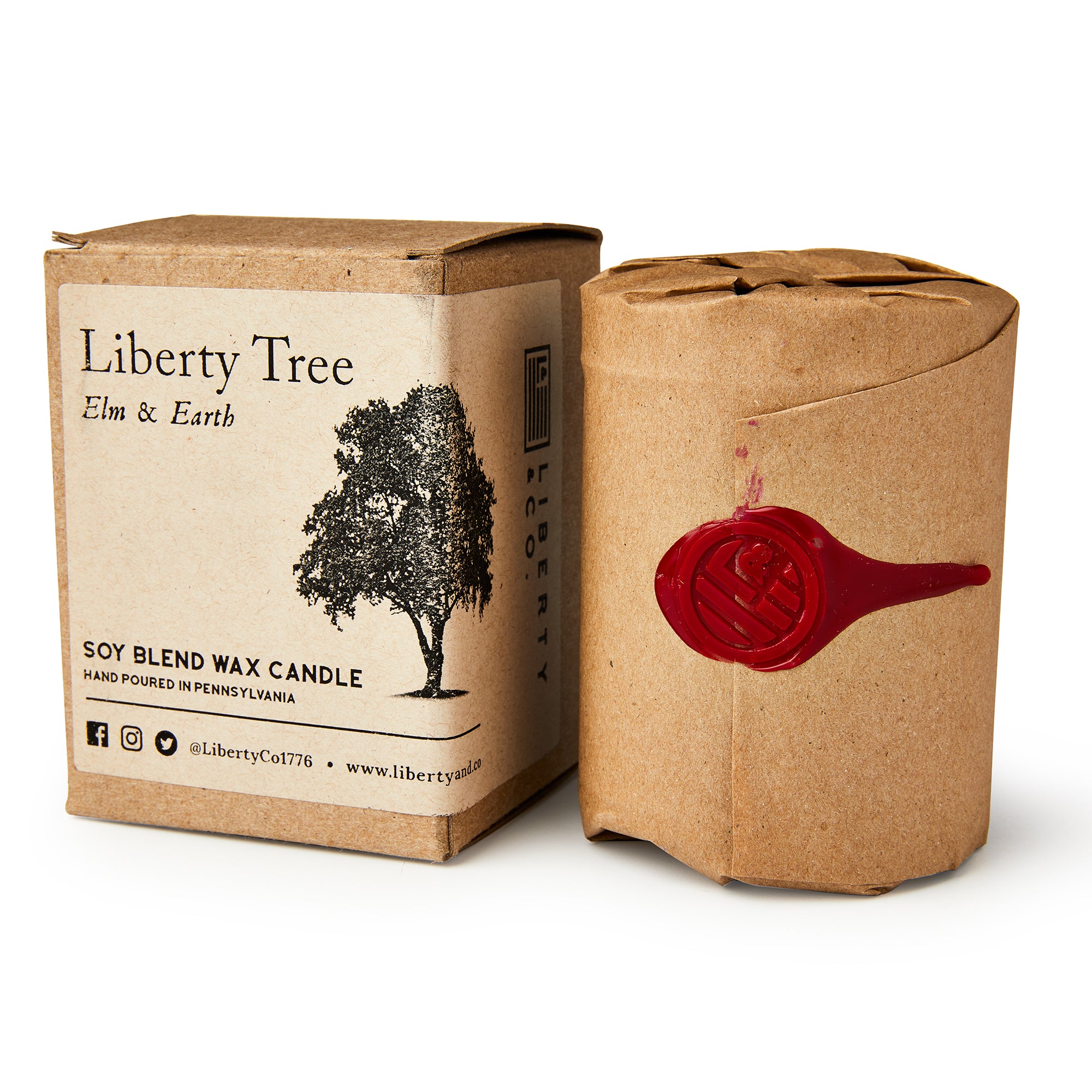 A Liberty Tree Candle with an elm and earth scent is wrapped in brown paper with a red wax seal beside its box labeled “Liberty Tree Candle.” The box displays a tree illustration along with product details.