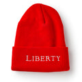 The Liberty Cap Beanie is a bright red beanie with a folded brim, featuring "LIBERTY" embroidered in white capital letters across the front.