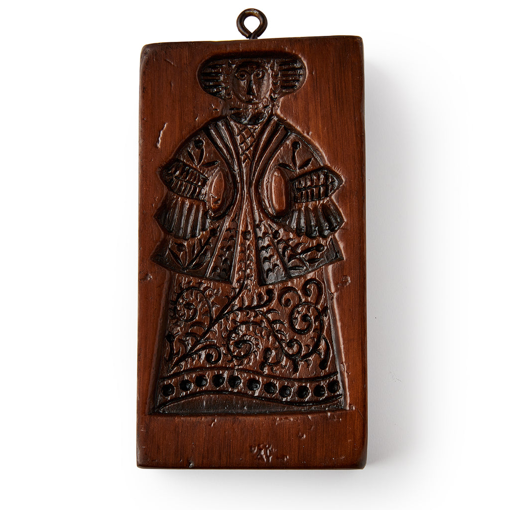 The Christopher Ludwick Gingerbread Mold, Small, Woman features a rectangular carved wooden design of a woman in colonial attire with a hat and patterned skirt, plus a top loop for hanging.