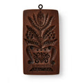 The Christopher Ludwick Gingerbread Mold, Small, Flower features a rectangular wooden design with a carved stylized flower bouquet in a vase and a hanging ring.