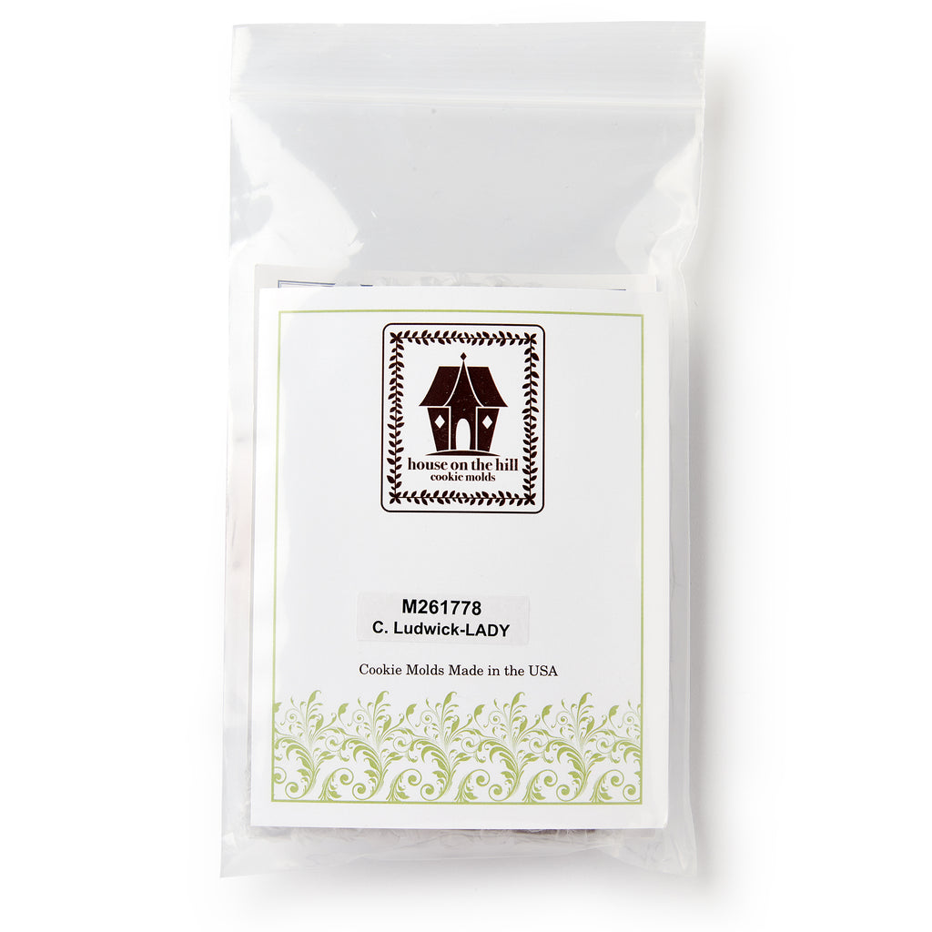 A clear plastic bag contains the Christopher Ludwick Gingerbread Mold, Small, Woman — with a house logo and green scrollwork — honoring colonial American baking traditions. 