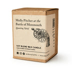 The Molly Pitcher Candle by Liberty Co. is a citrus-scented soy candle, hand-poured in Pennsylvania, packaged in a brown box featuring a cannon illustration and American Revolution-inspired design.