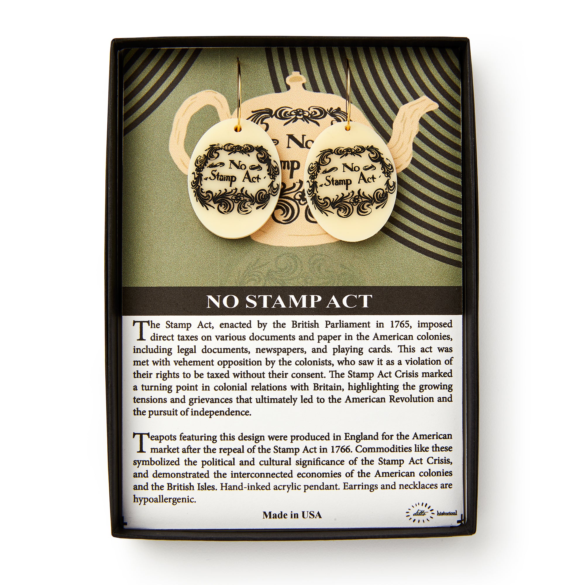 The No Stamp Act Earrings come in a box with an insert explaining the Stamp Act’s history. These round, cream-colored earrings feature ornate black designs and "No Stamp Act" text as a symbol of colonial protest.
