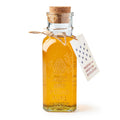 A clear glass bottle of Wildflower Honey, sealed with a cork and twine tag reading “Museum of the American Revolution,” features an embossed beehive design and the words “One Pound Pure Honey.”.