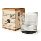A clear whiskey glass with white etched "Join or Die" text and designs, inspired by Benjamin Franklin, sits beside a brown box labeled Join or Die Whiskey Glass by Liberty Co., featuring vintage-style typography and decorative accents.