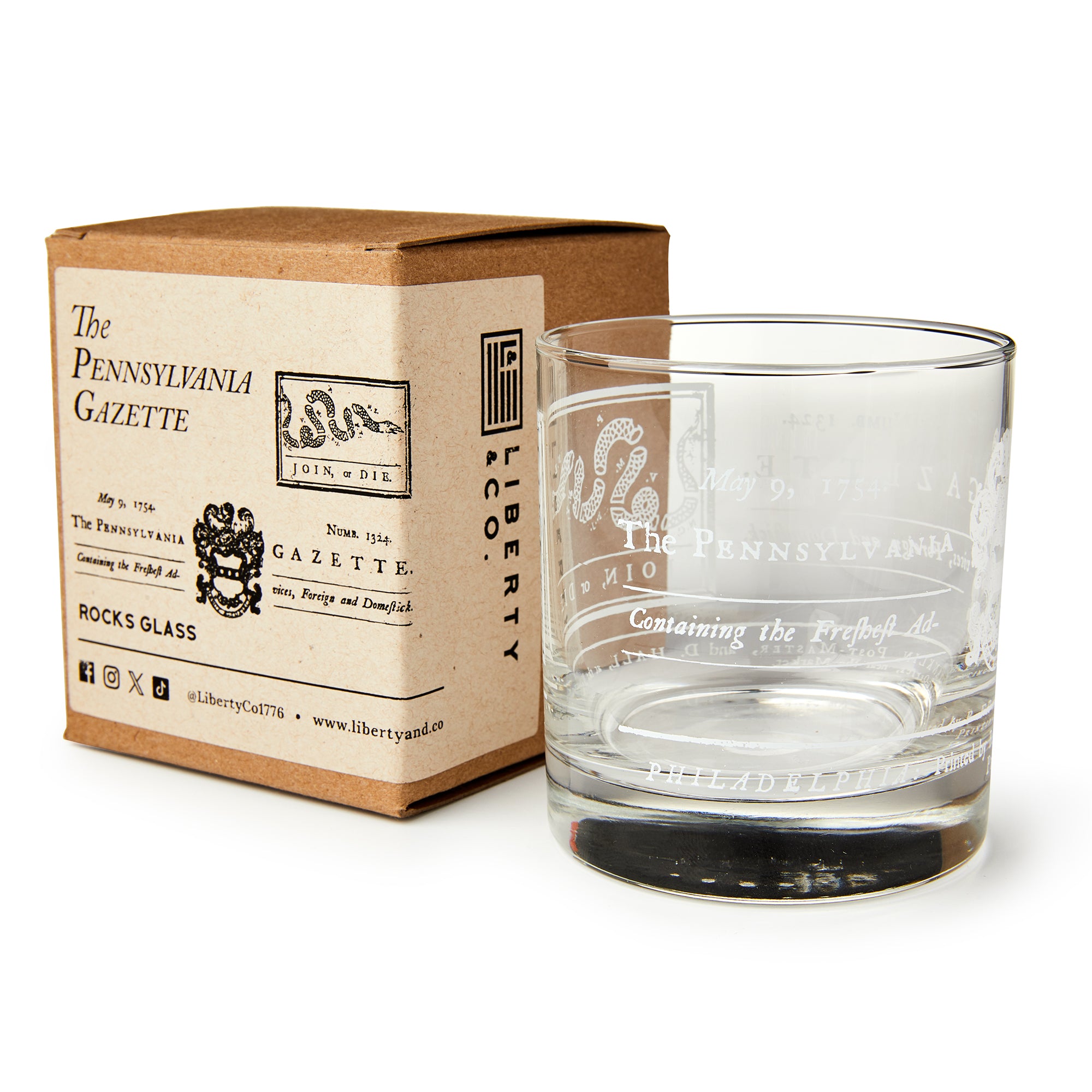 A clear whiskey glass with white etched "Join or Die" text and designs, inspired by Benjamin Franklin, sits beside a brown box labeled Join or Die Whiskey Glass by Liberty Co., featuring vintage-style typography and decorative accents.
