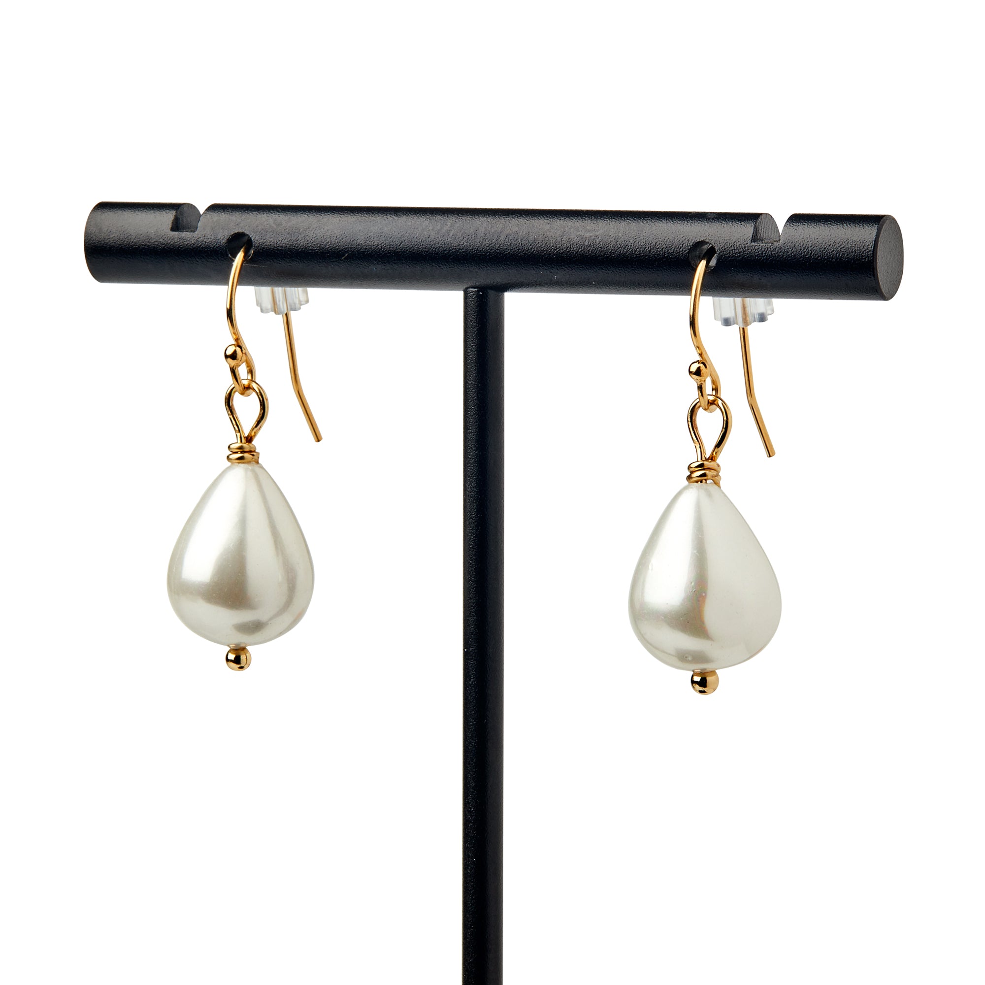 The Pearl Earrings in Gold feature elegant teardrop-shaped white pearls on gold hooks, displayed on a black stand against a white background for a timeless appearance.