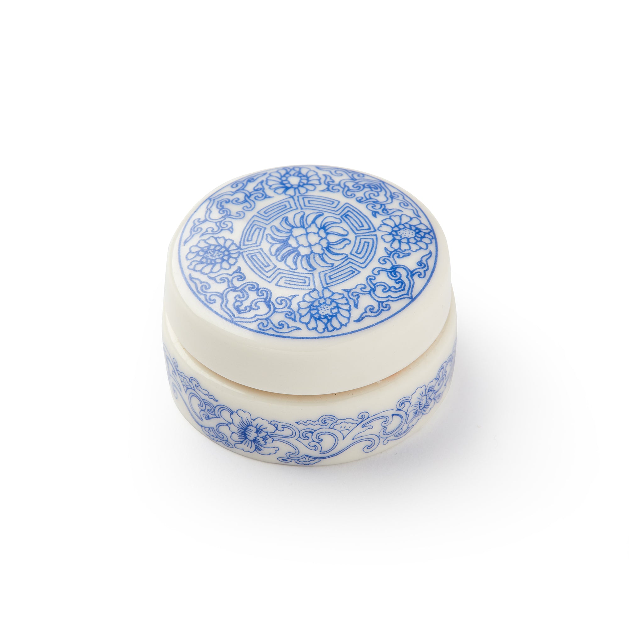 Crème Rouge comes in a small, round porcelain pot with a blue and white floral pattern inspired by traditional designs, ideal for a natural flush. Displayed against a white background.