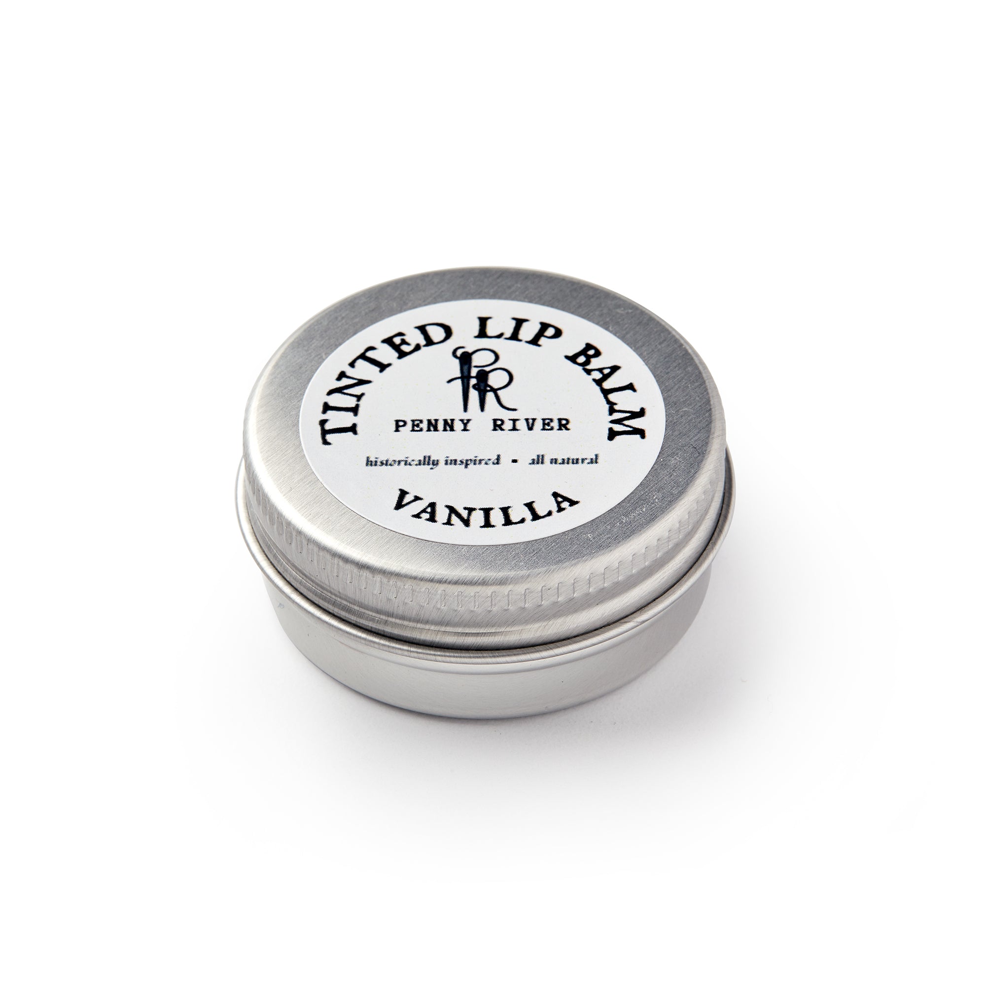 A small, round metal tin labeled Lip Balm Vanilla by Penny River sits closed on a white background. The lid features the text "historically inspired • all natural." This is a moisturizing tinted lip balm.