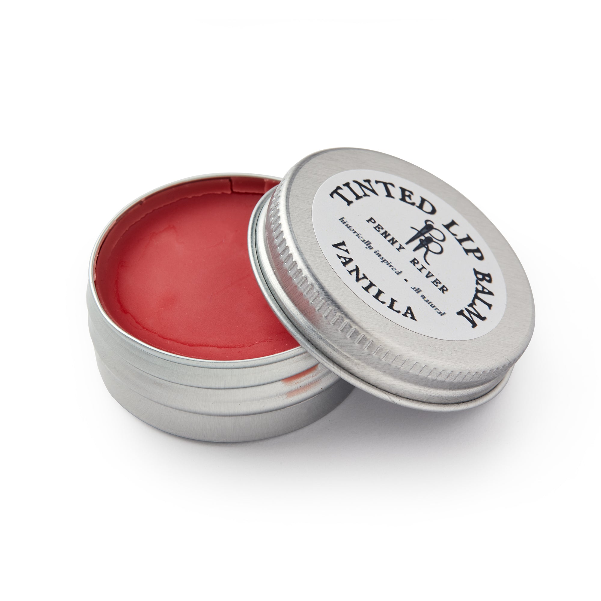 A small round tin of Lip Balm in a moisturizing red shade. The lid, labeled "Tinted Lip Balm, Penny River, Vanilla," is partially open to show the balm inside.