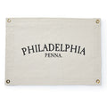 The Philadelphia Canvas Banner is a cream-colored rectangular flag with metal grommets in each corner and bold black arched “PHILADELPHIA PENNA.” text.