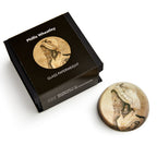 A round glass paperweight featuring an illustration of African American poet Phillis Wheatley, shown beside its black box labeled "Phillis Wheatley Glass Paperweight" from the Museum of the American Revolution.