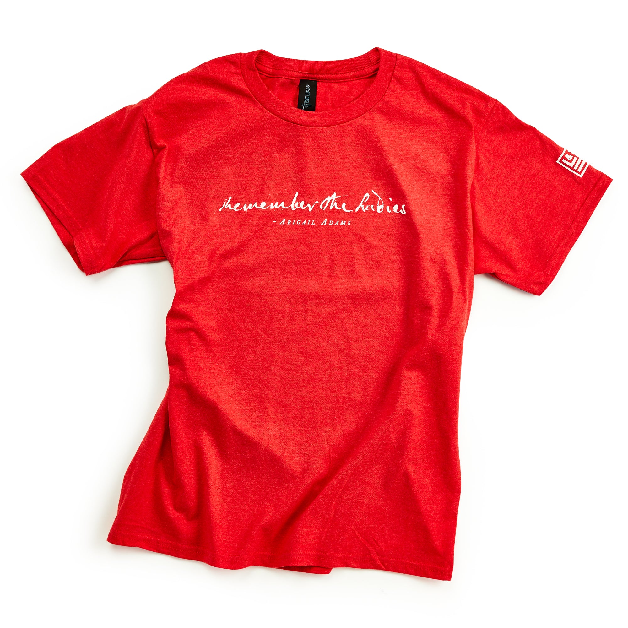 The Remember the Ladies T-Shirt, Youth, is a red tee with white cursive text on the chest reading "heaven but the ladies and Adrienne Rich," honoring women's rights. It also features a small white design on the left sleeve.