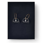 Skull and Crossbone Earrings: Clear acrylic earrings with gold hoops, each featuring a white skull-and-crossbones design, displayed on black—ideal for fans of historical or Stamp Act-inspired jewelry.