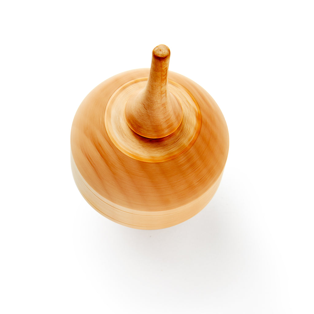 A Wooden Top is photographed from above on a white background, with motion blur around the edges emphasizing this handcrafted classic toy in action.