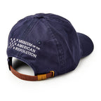 The Star Cap is a navy cotton twill hat with "Museum of the American Revolution" and white stars embroidered on the back. It features an adjustable brown leather strap with a brass buckle.
