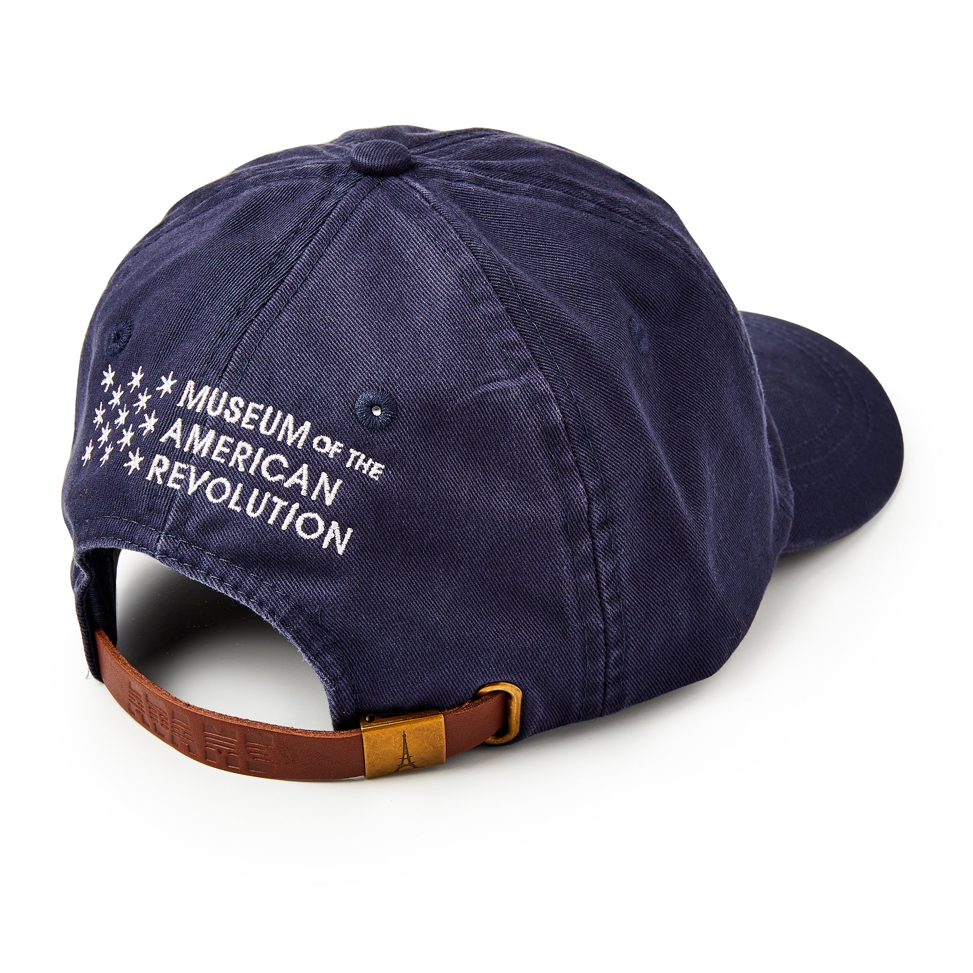 The Star Cap is a navy cotton twill hat with "Museum of the American Revolution" and white stars embroidered on the back. It features an adjustable brown leather strap with a brass buckle.