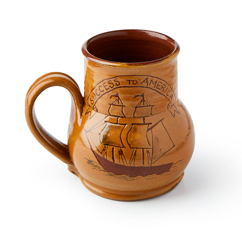 The "Success to America" Ship Mug is a brown redware ceramic mug with a large handle, featuring an illustration of a sailing ship and a banner reading SUCCESS TO AMERICA.