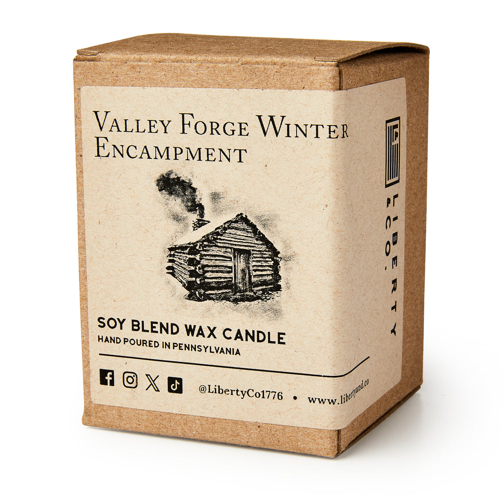 A brown box labeled Valley Forge Winter Encampment features a log cabin sketch. Inside is the Valley Forge Candle—a hand-poured soy blend by Liberty Candle Co., crafted in Pennsylvania for a warm, historical ambiance. Social media icons included.