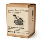 A brown box labeled Valley Forge Winter Encampment features a log cabin sketch. Inside is the Valley Forge Candle—a hand-poured soy blend by Liberty Candle Co., crafted in Pennsylvania for a warm, historical ambiance. Social media icons included.
