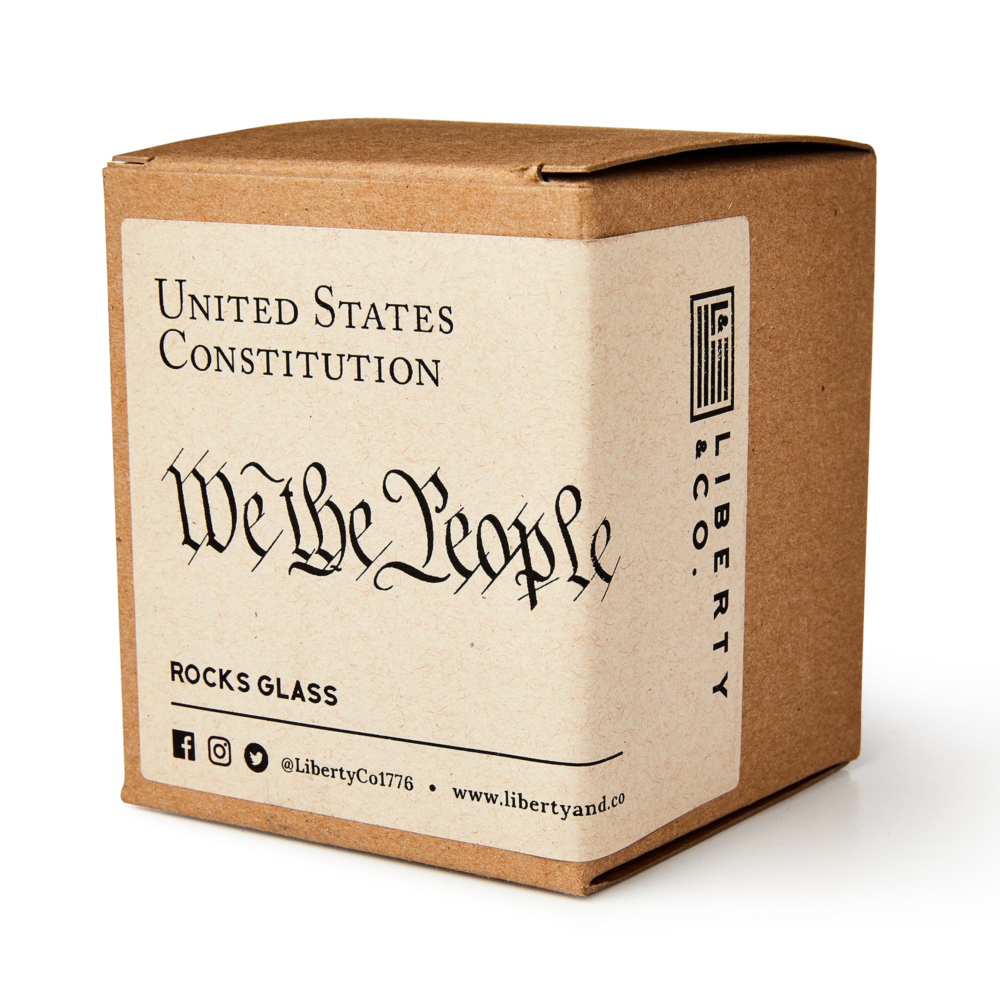 A brown cardboard box labeled "We The People Whiskey Glass" from Liberty & Co., containing the whiskey glass, with social media icons and the company website on the packaging.