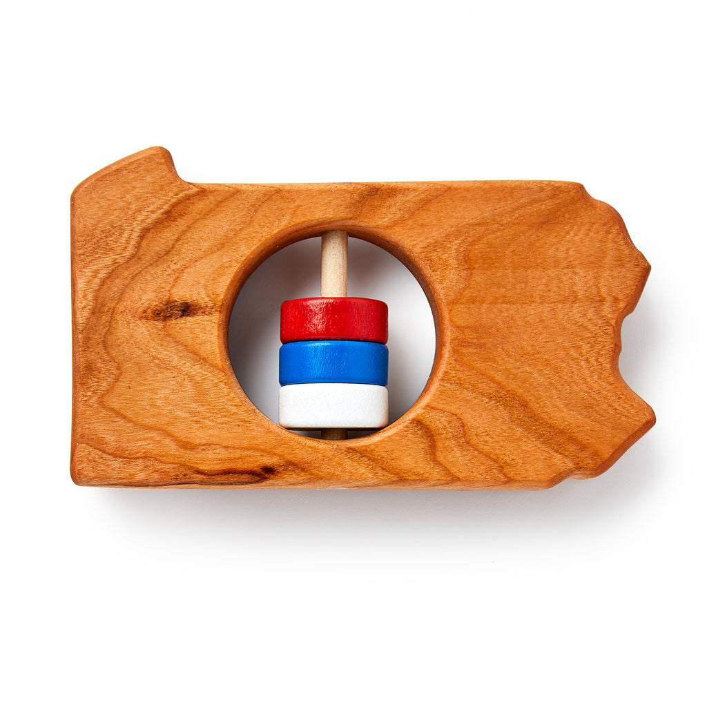 The Pennsylvania State Wooden Rattle is a handcrafted wooden baby toy shaped like Pennsylvania, with a circular cutout and spindle holding red, white, and blue rings.