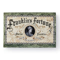 A decorative game box labeled “Franklin’s Fortune Deck Building Game,” adorned with ornate scrollwork and a central portrait of Benjamin Franklin.