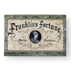A decorative game box labeled “Franklin’s Fortune Deck Building Game,” adorned with ornate scrollwork and a central portrait of Benjamin Franklin.