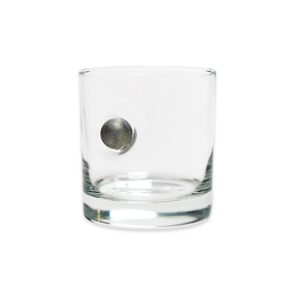 The Musket Ball Rocks Glass, handcrafted in the USA from clear glass and featuring a metallic musket ball-inspired sphere embedded in its side, is displayed against a plain white background.