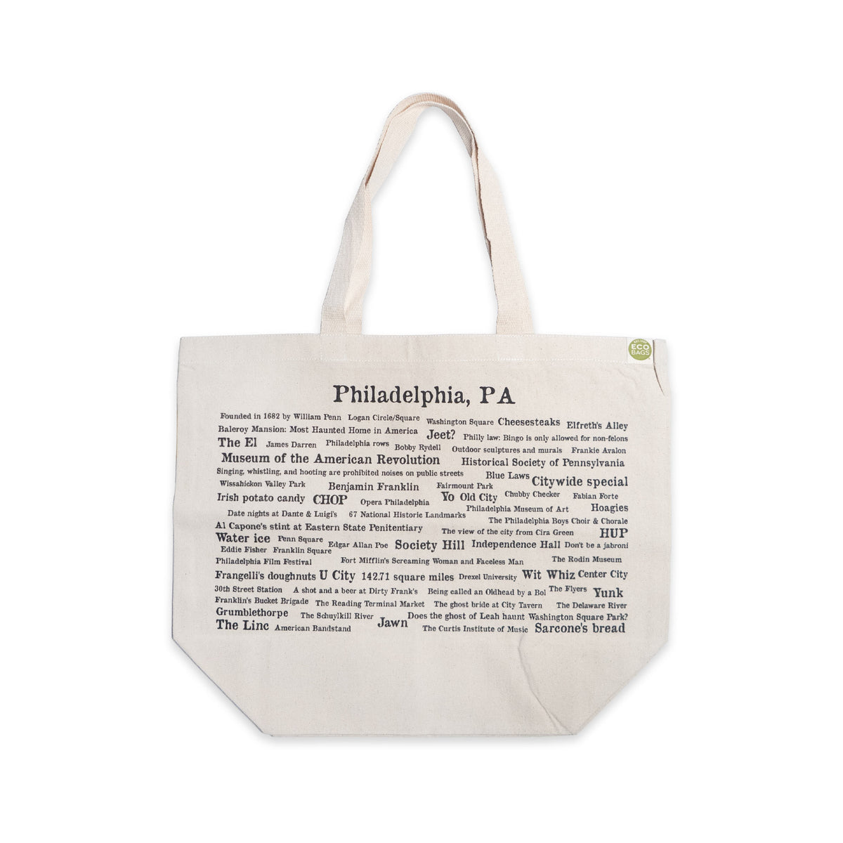 The Philadelphia Pride Ecotote is a beige cotton canvas tote bag featuring “Philadelphia, PA” at the top and black printed names of city landmarks, streets, and Philly trivia phrases arranged in various fonts and sizes. This Philadelphia tote includes two sturdy handles and a small green tag.