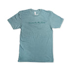 A light blue short-sleeve Remember the Ladies T-Shirt (MoAR) featuring “remember the lilies” and “Jasmin Arora” in delicate cursive across the chest, inspired by iconic women’s rights figures. The commemorative tee is displayed flat on a white background.