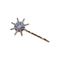 The Antiqued Star Barrette is a gold hairpin featuring a starburst design adorned with small, sparkling rhinestones, creating a celestial accessory that evokes timeless elegance against a white background.