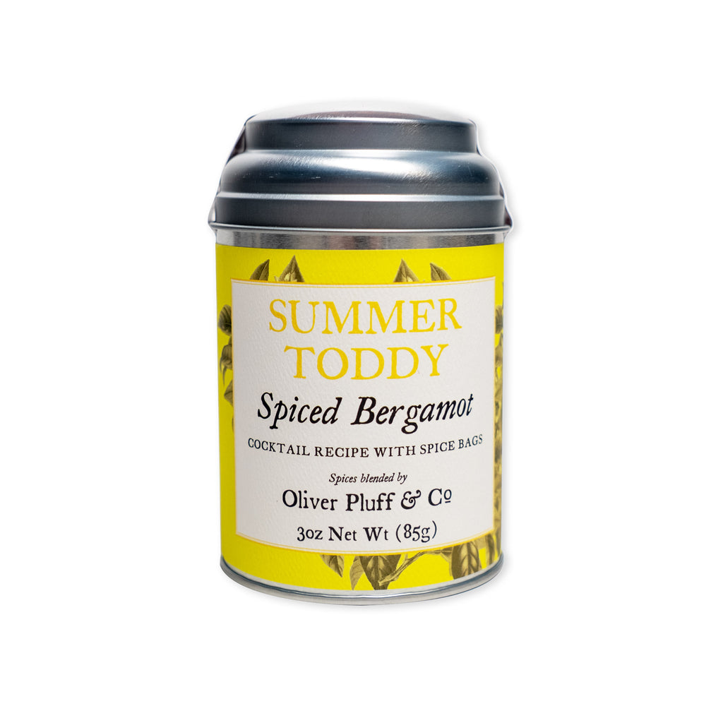 A yellow and white metal tin labeled "Summer Toddy, Spiced Bergamot" with black text and a silver lid contains cocktail spice bags featuring a vibrant aromatic spice blend. Perfect for crafting a flavorful non-alcoholic beverage, the net weight is 3 oz (85g).