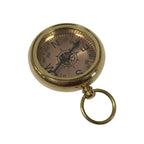 The Solid Polished Brass Pocket Compass features a ring attachment, black needle, and marked cardinal directions on its face, making it both a reliable navigation tool and an elegant decorative piece against a white background.