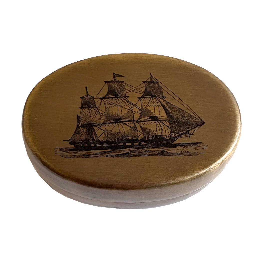 The Sailing Ship Pill Box is a round, antiqued brass container featuring an engraved sailing ship on the lid, shown from above against a white background.