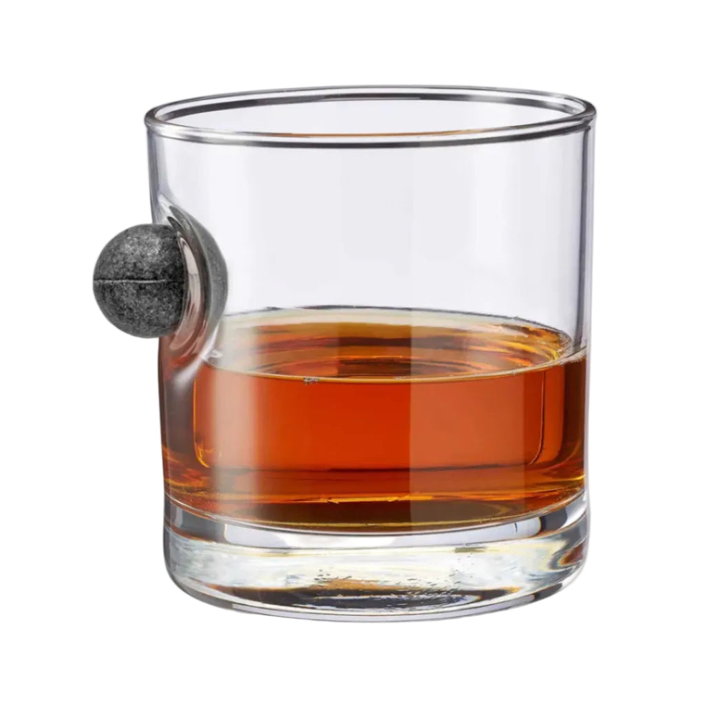 The Musket Ball Rocks Glass features a gray stone sphere embedded in the side and is inspired by musket ball glasses, making it a striking handcrafted piece that stands out against a white background.