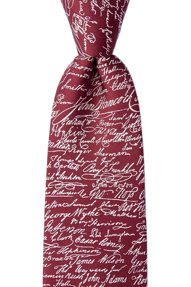 A close-up of the Declaration of Independence Signers Silk Tie showcases its maroon silk fabric adorned with white cursive signatures, forming a distinctive all-over pattern. Knotted and set against a plain white background, this tie makes a perfect gift for history enthusiasts or a stylish accessory for patriotic celebrations.