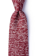 A close-up of the Declaration of Independence Signers Silk Tie showcases its maroon silk fabric adorned with white cursive signatures, forming a distinctive all-over pattern. Knotted and set against a plain white background, this tie makes a perfect gift for history enthusiasts or a stylish accessory for patriotic celebrations.