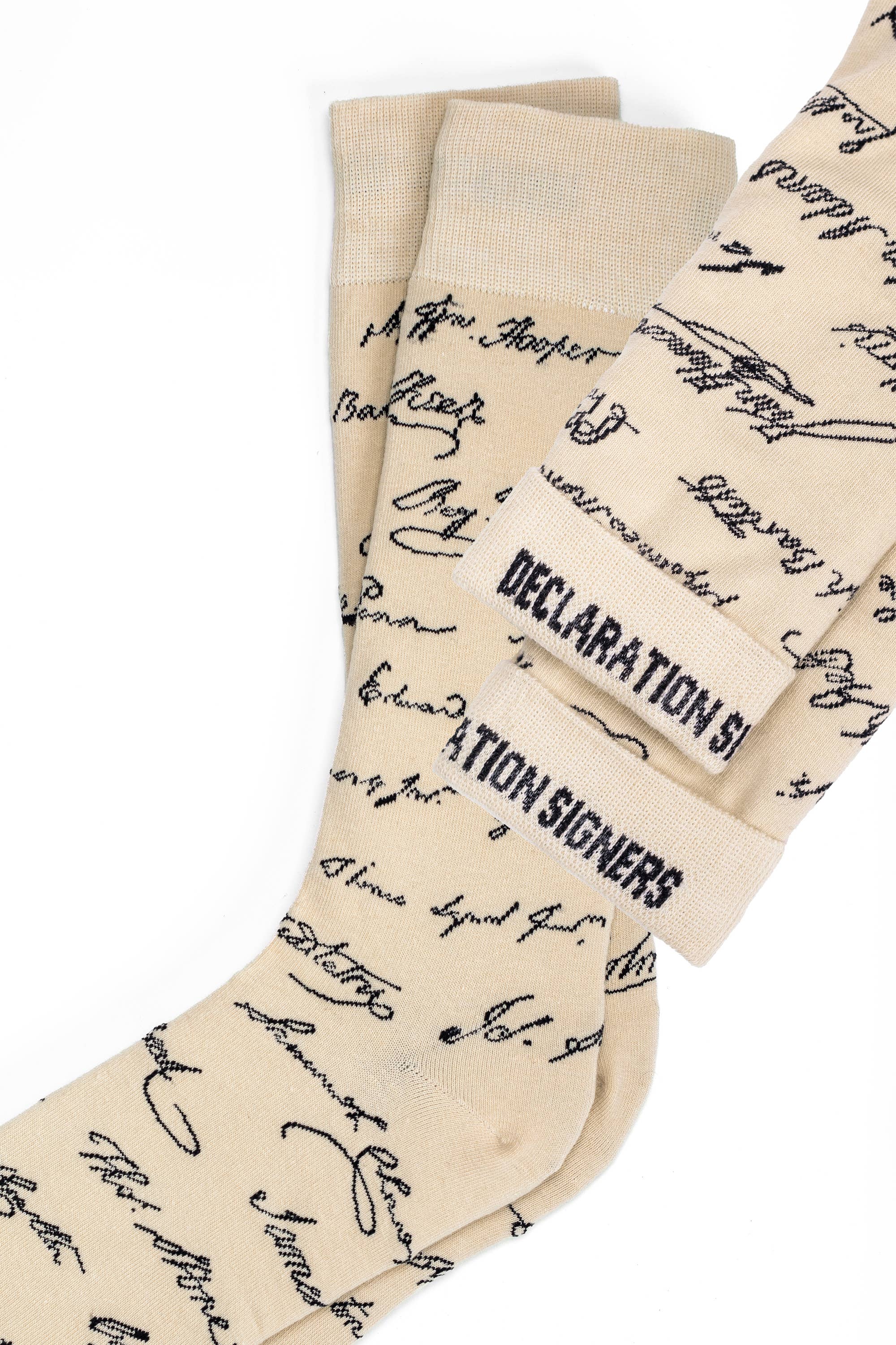 Declaration Signers Crew Socks feature a beige design with black cursive text reminiscent of authentic historical signatures, evoking the spirit of the Declaration of Independence. The bold "DECLARATION SIGNERS" text on the cuffs adds a striking touch, making these socks ideal for anyone who values handwritten documents and American history.