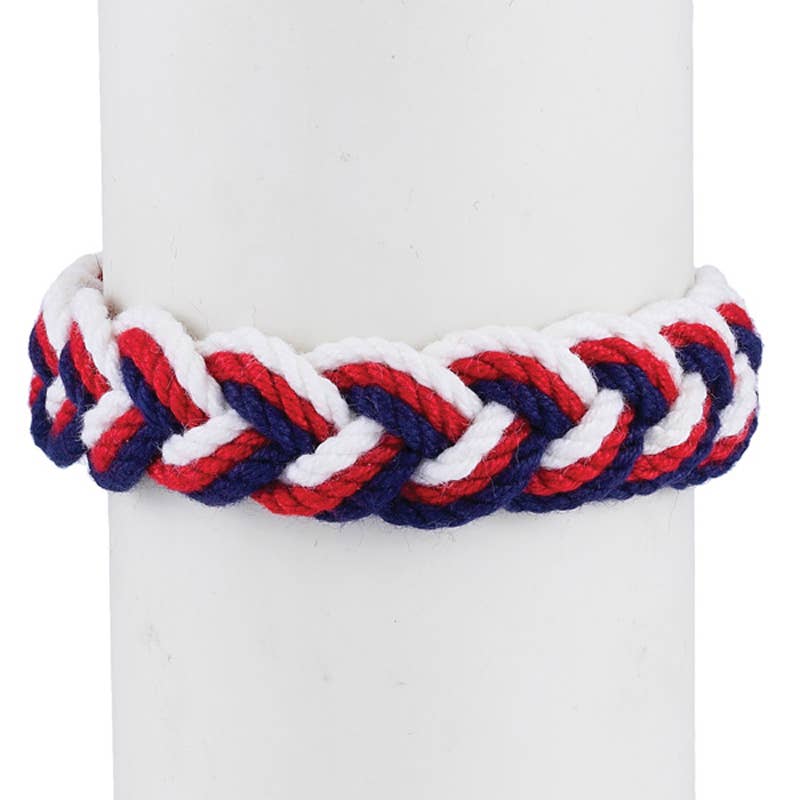 A Red, White & Blue Sailor Knot Bracelet featuring repeating red, white, and blue rope strands wrapped around a white display cylinder to evoke maritime heritage.