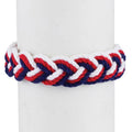 A Red, White & Blue Sailor Knot Bracelet featuring repeating red, white, and blue rope strands wrapped around a white display cylinder to evoke maritime heritage.