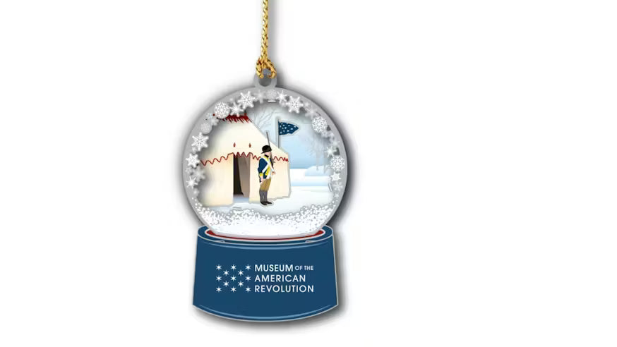 Celebrate history with the George Washington's Tent Ornament — a holiday snow globe featuring a Revolutionary War soldier and flag outside a white hut, with “Museum of the American Revolution” on the blue base.